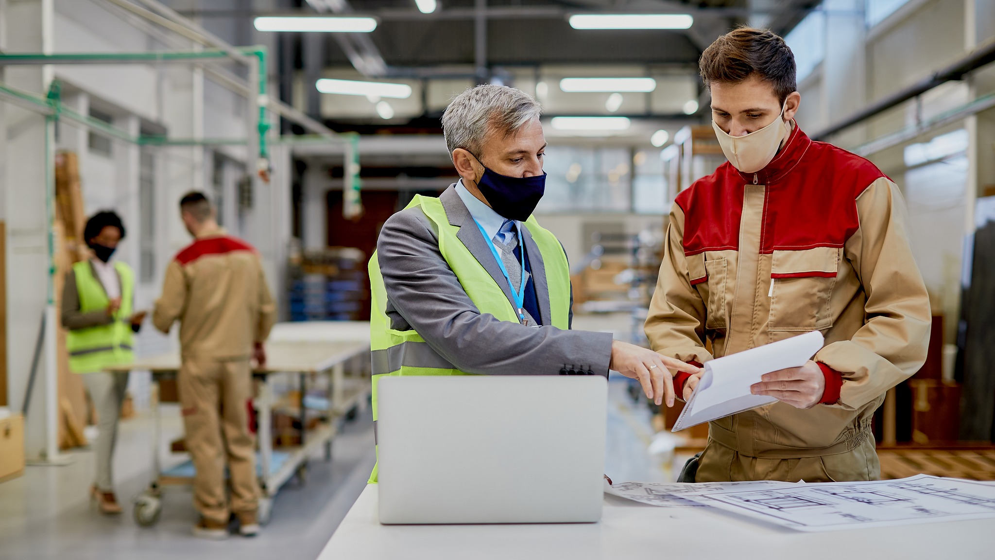 Two men in protective clothing operate machinery in a factory setting, focused on their tasks for safety and efficiency.