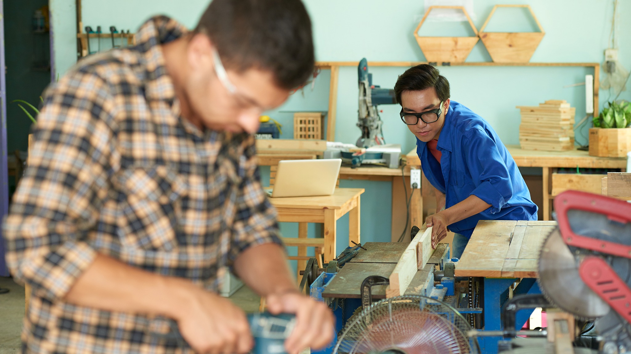 A man focused on a woodworking project, using tools to shape wood in a well-lit workshop.